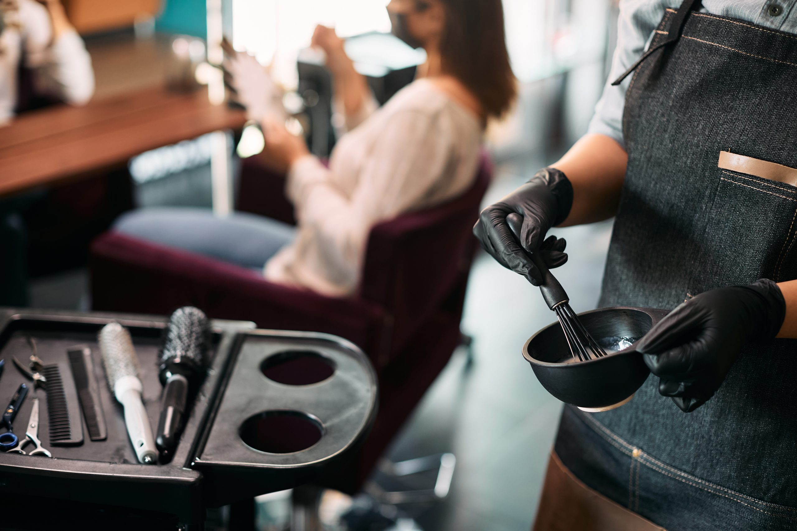 Close-up of hairdresser preparing dye in a container at hair salon.